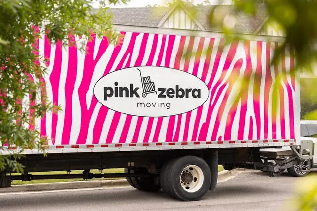 A pink zebra moving truck driving down the street.